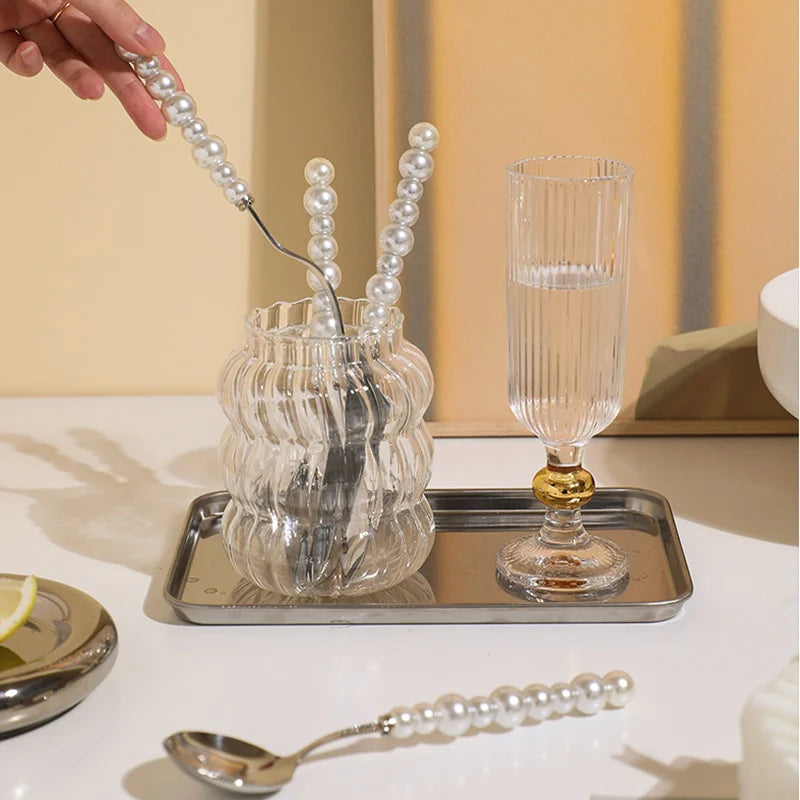Clear glass with gold base on a tray, surrounded by decorative items on a table.