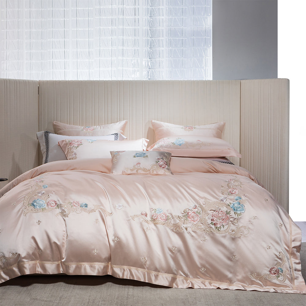 Pink floral embroidered bedding set on a bed with a neutral headboard.