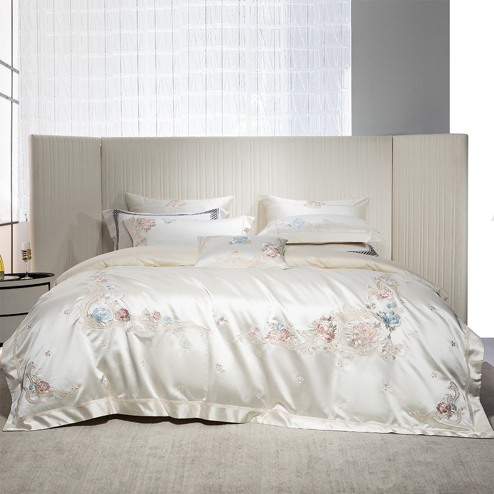 White embroidered bedding set on a bed with a neutral headboard.