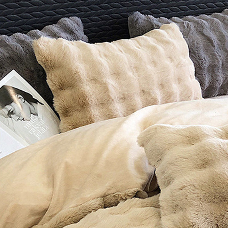 Close-up of fluffy beige pillows and blanket on a bed with a blurred background