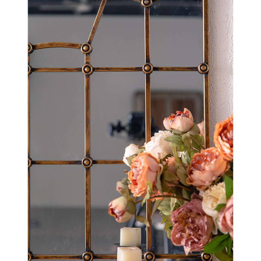 Decorative window pane mirror with floral arrangement and candles in front of a window.