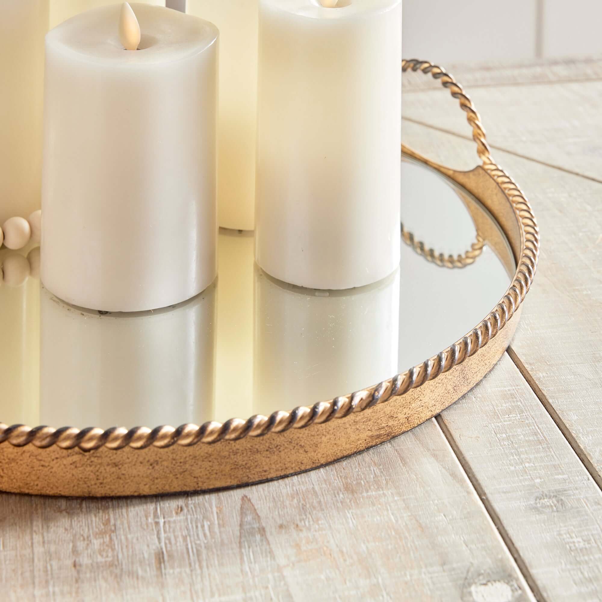 Two white candles on a decorative gold tray on a wooden surface