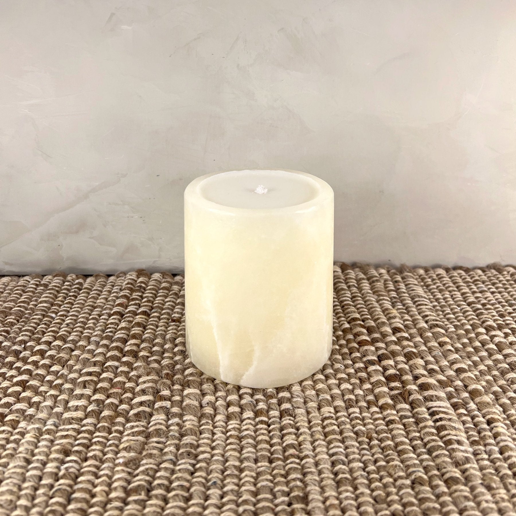 Flickering candle in a glass holder on a textured surface with a neutral background