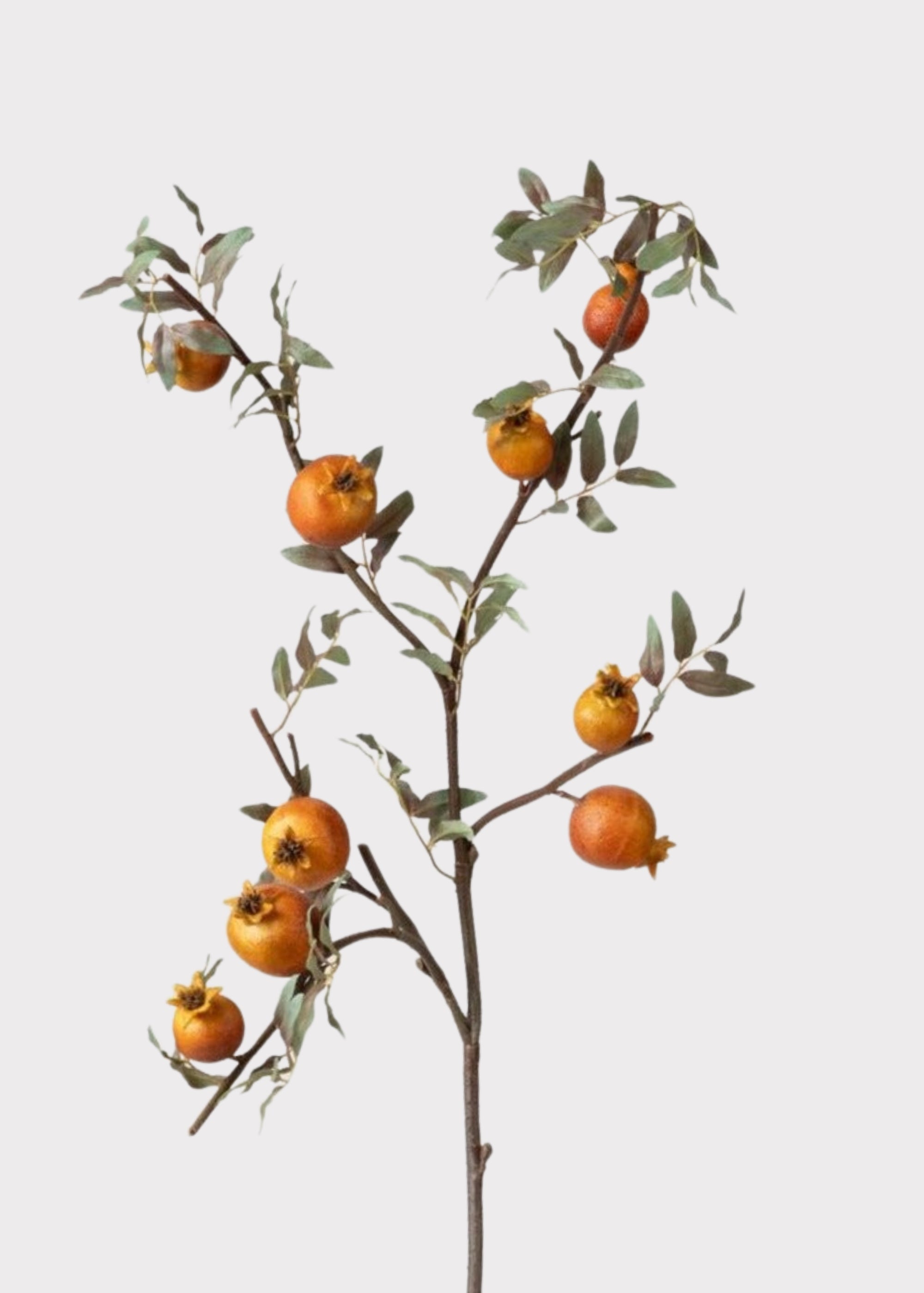 Artificial pomegranate branch with orange fruits on a light gray background