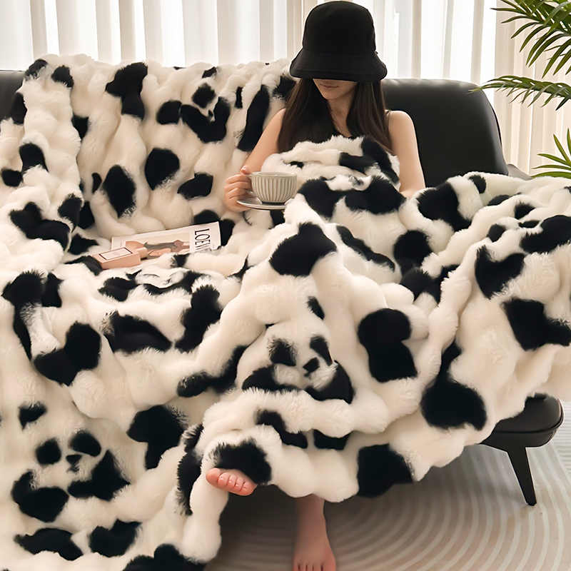 Person sitting on a couch under a black and white panda blanket, holding a bowl.