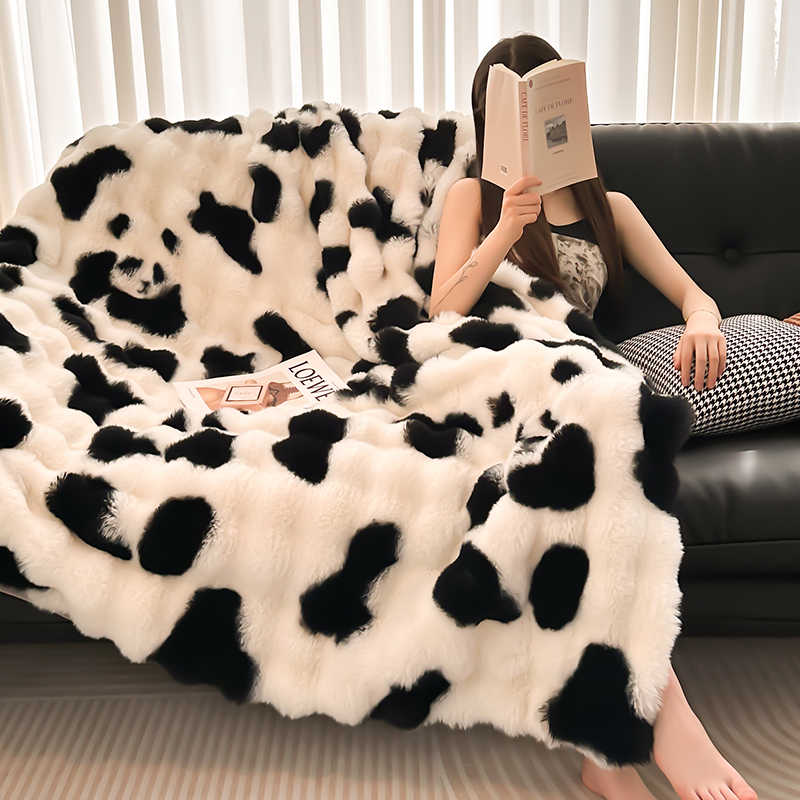 Person sitting on a couch under a panda print blanket, holding a book.