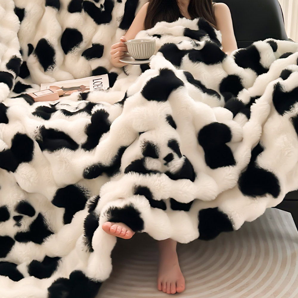 Person wrapped in a black and white panda blanket holding a cup and a magazine.