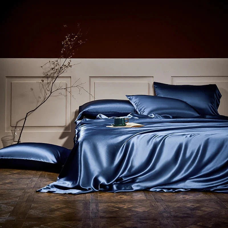 Blue satin bedding set on a bed in a dimly lit room.