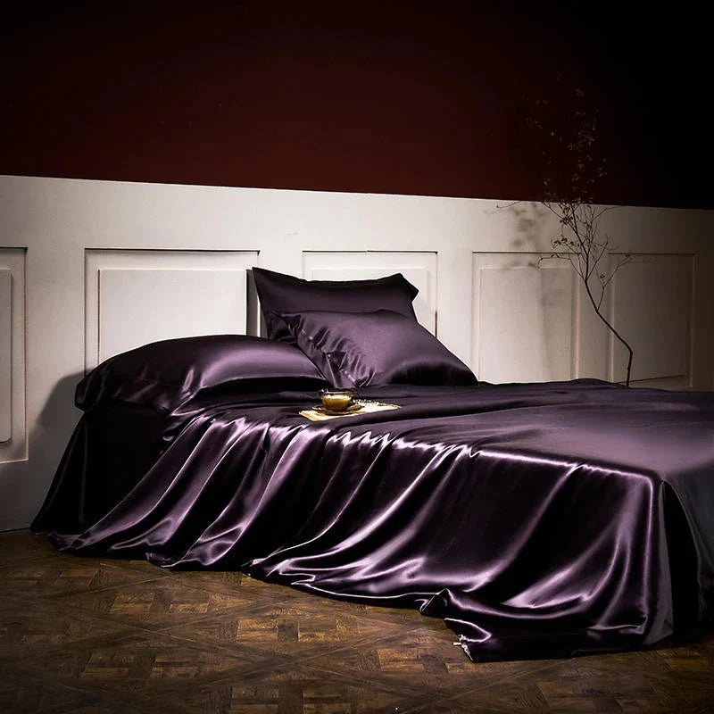 Purple satin bedding set on a bed in a dimly lit room.