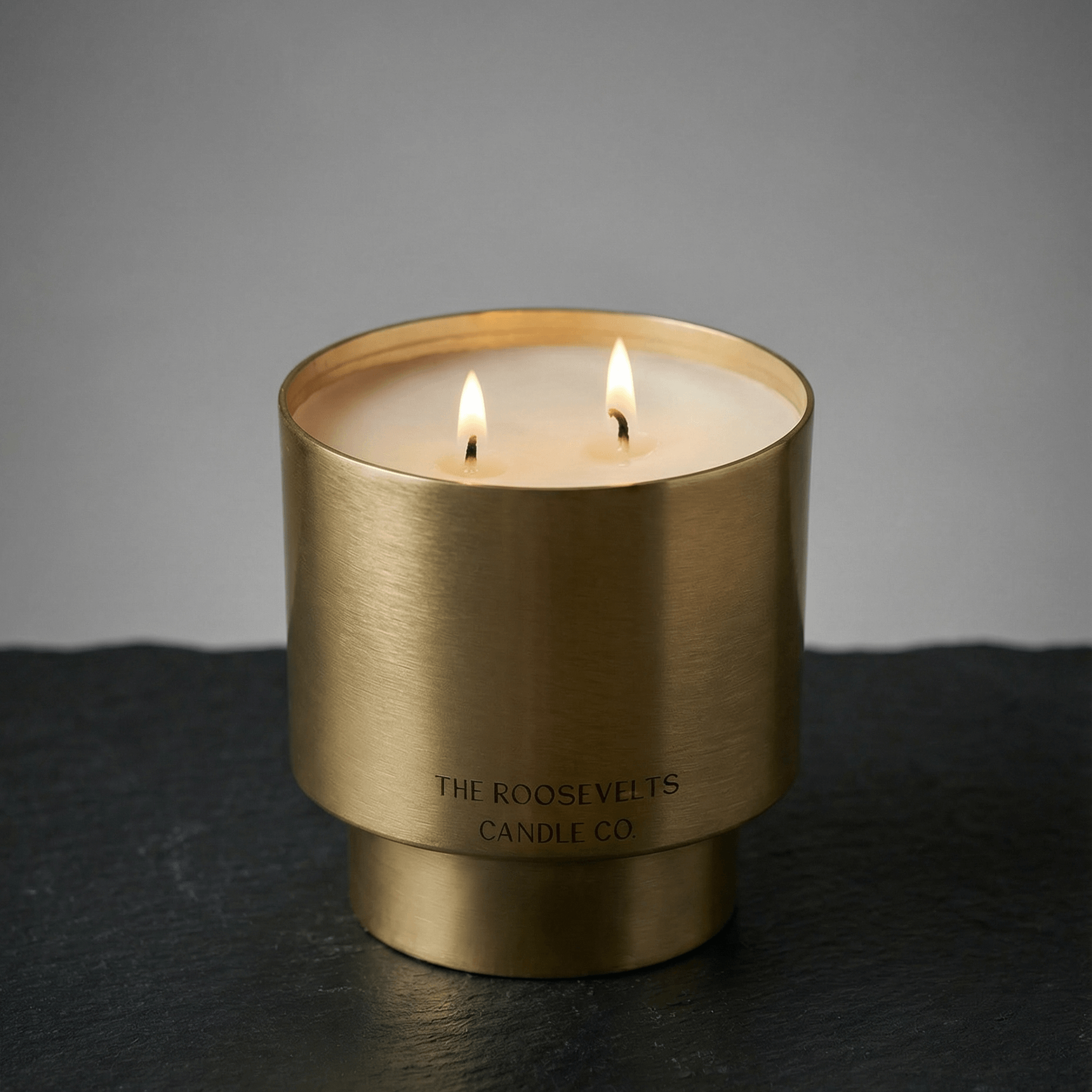 Gold candle holder with two lit candles on a dark surface and gray background