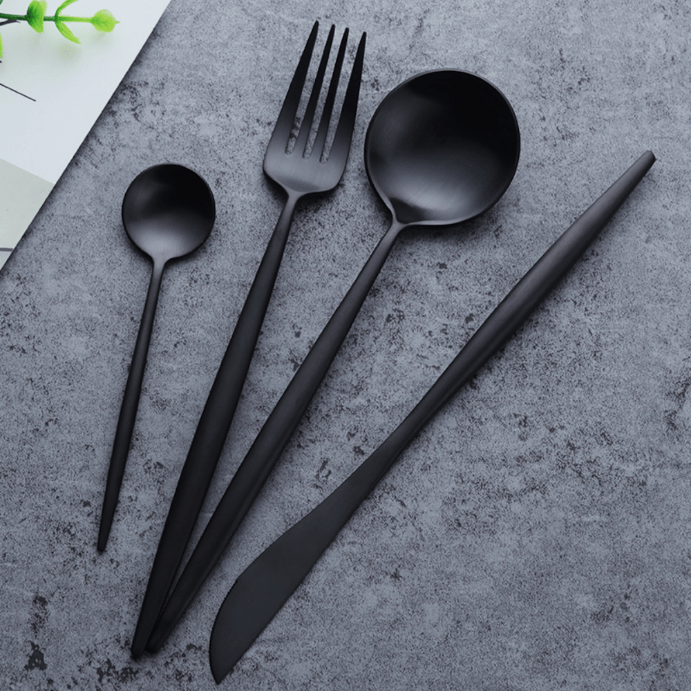 Set of black cutlery including a fork, knife, and two spoons on a gray surface.