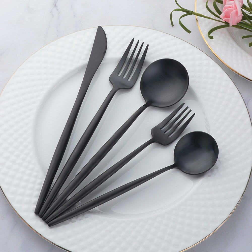 Set of black cutlery on a white plate with a floral arrangement in the background.