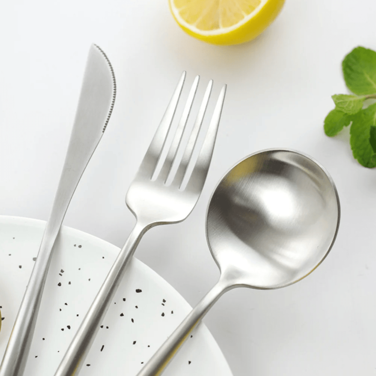 Stainless steel cutlery set on a white surface with a lemon and mint leaves.