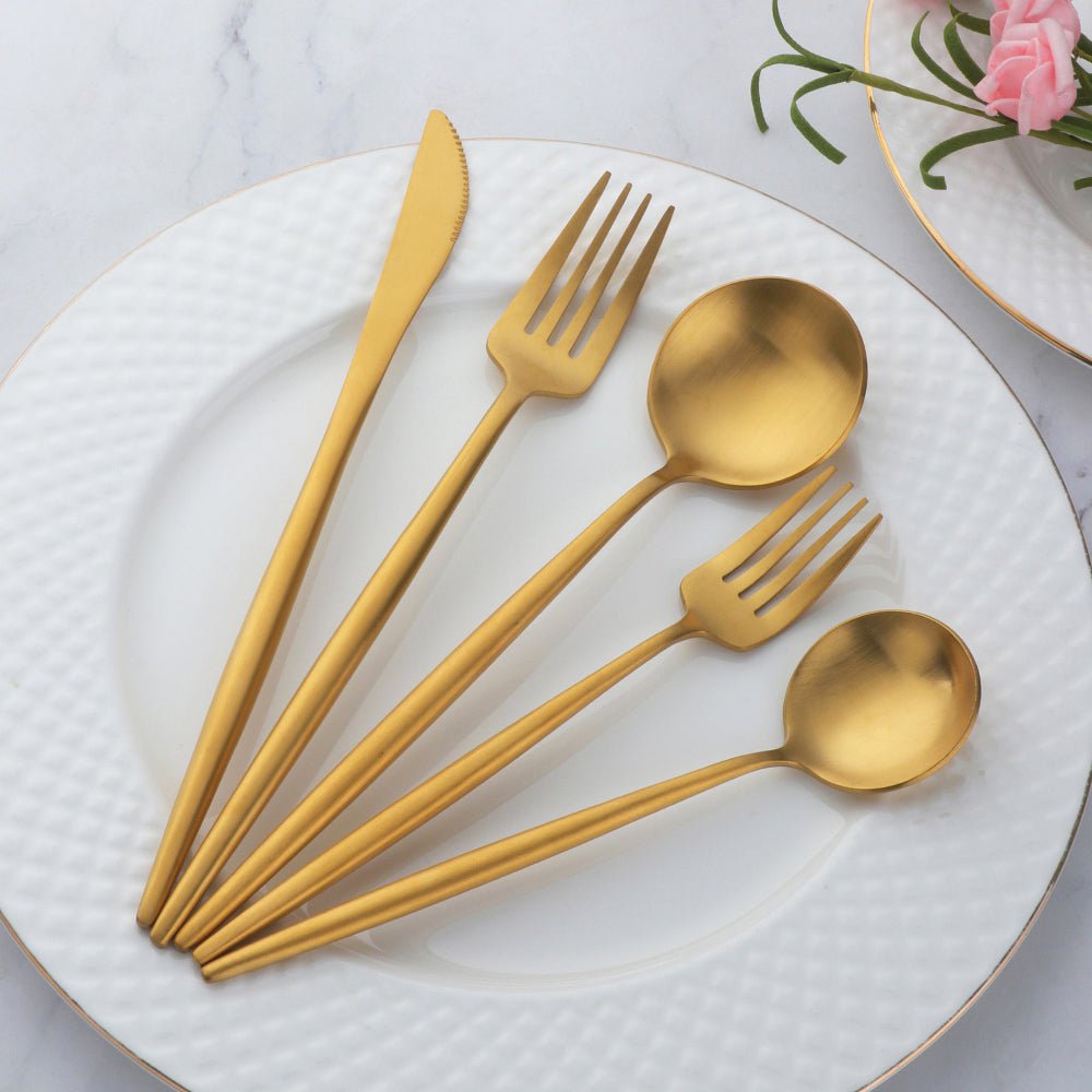 Set of gold cutlery on a white plate with a marble background