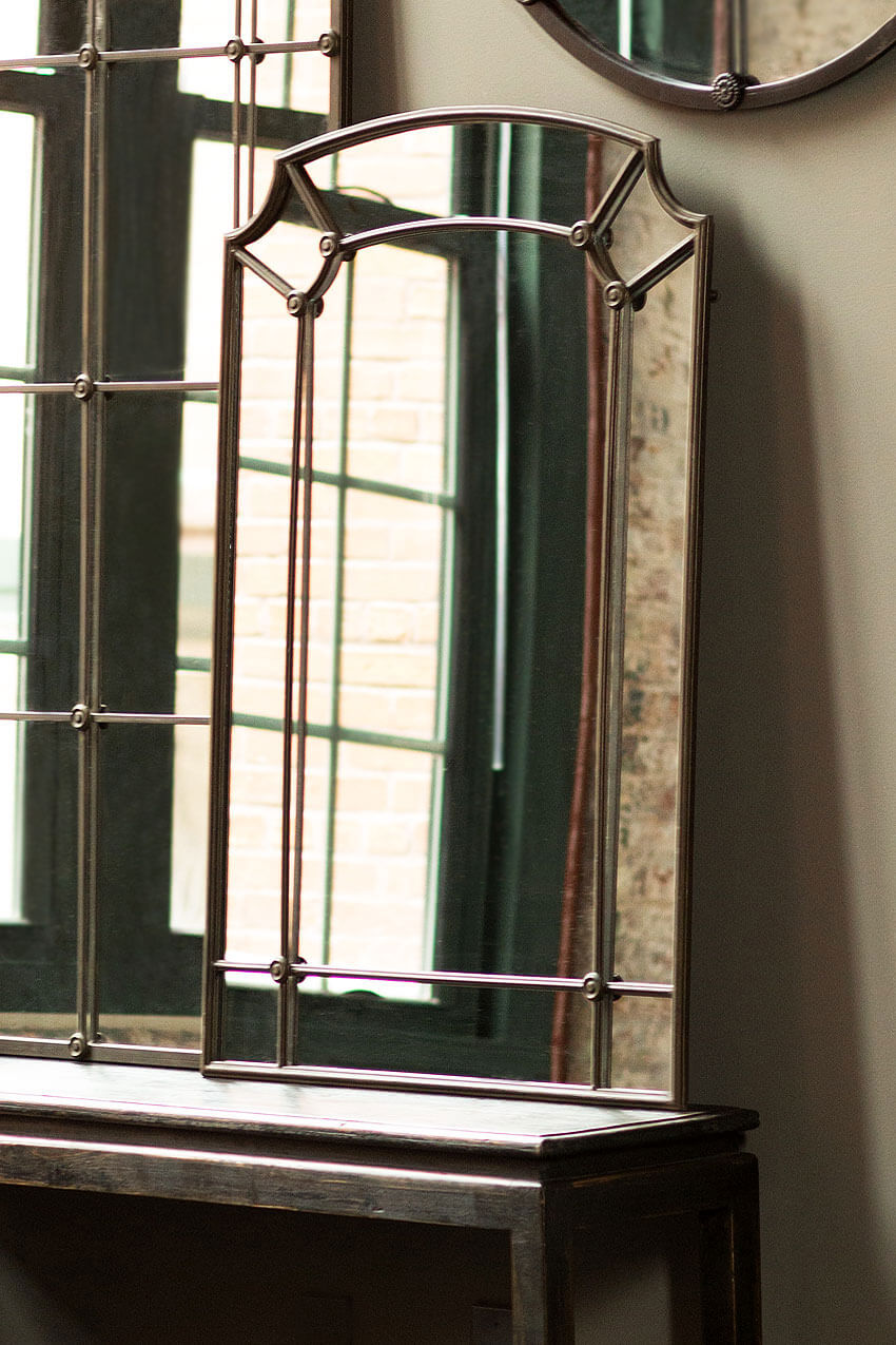 Decorative mirror with intricate frame on a wooden surface near a window.