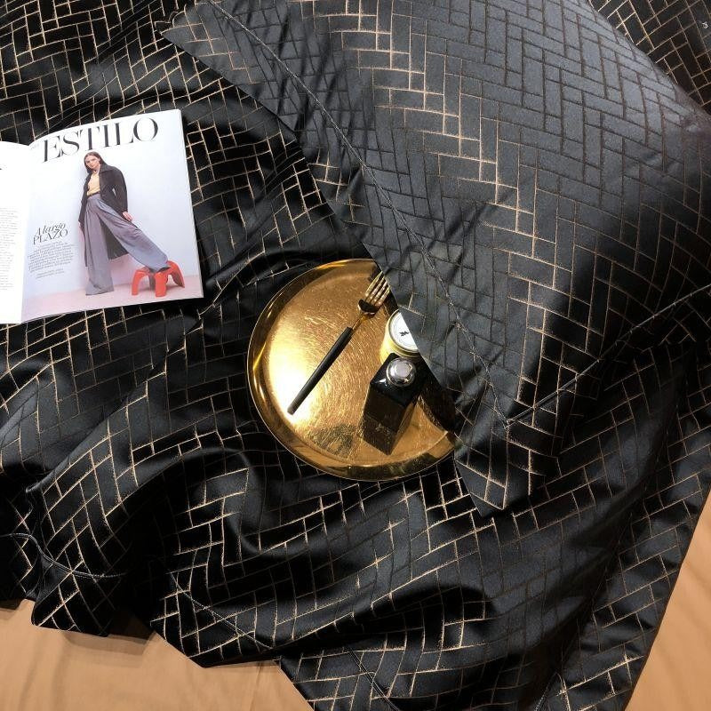 Black textured fabric with a gold geometric design, gold dish, pen, and magazine titled 'Estilo'.