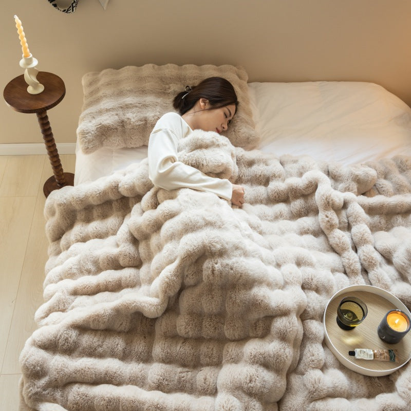 Person lying on a bed covered with a fluffy beige blanket in a cozy room.
