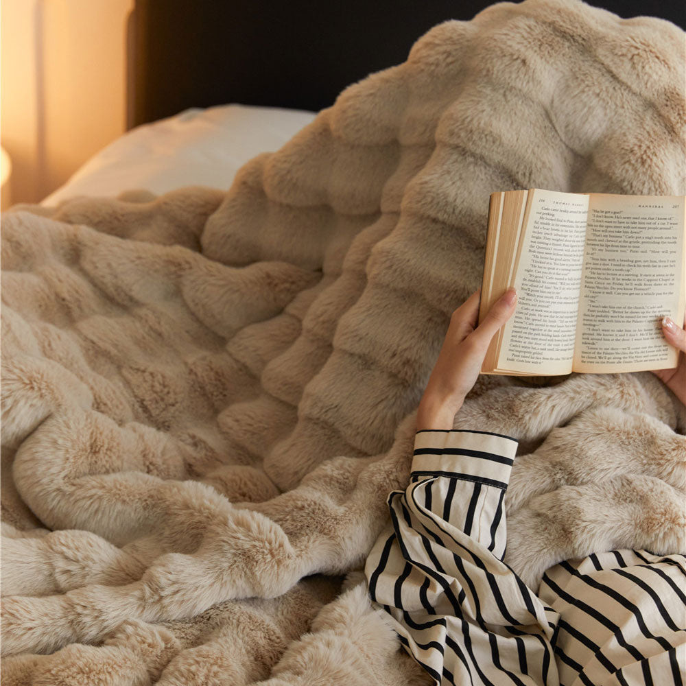 Person reading a book under a fluffy beige blanket in a cozy setting