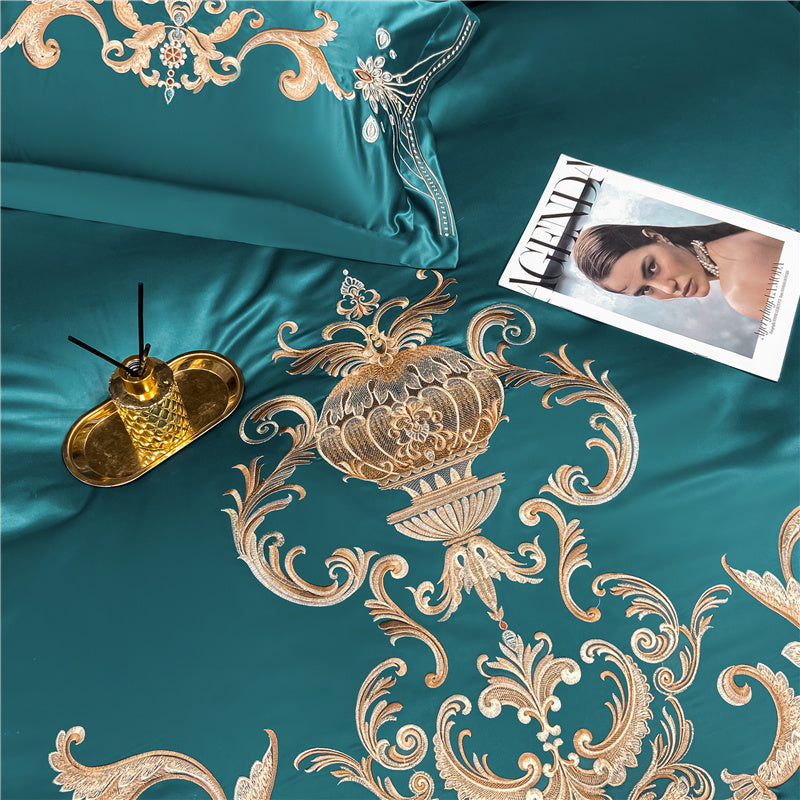 Teal bedspread with gold embroidery and decorative pillows on a bed.
