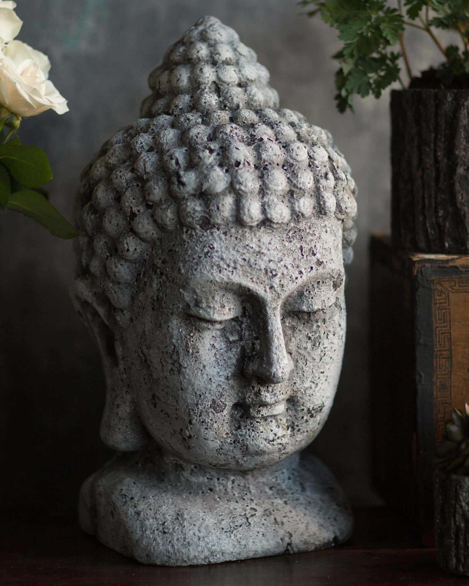 Stone Buddha head sculpture with flowers and books in the background