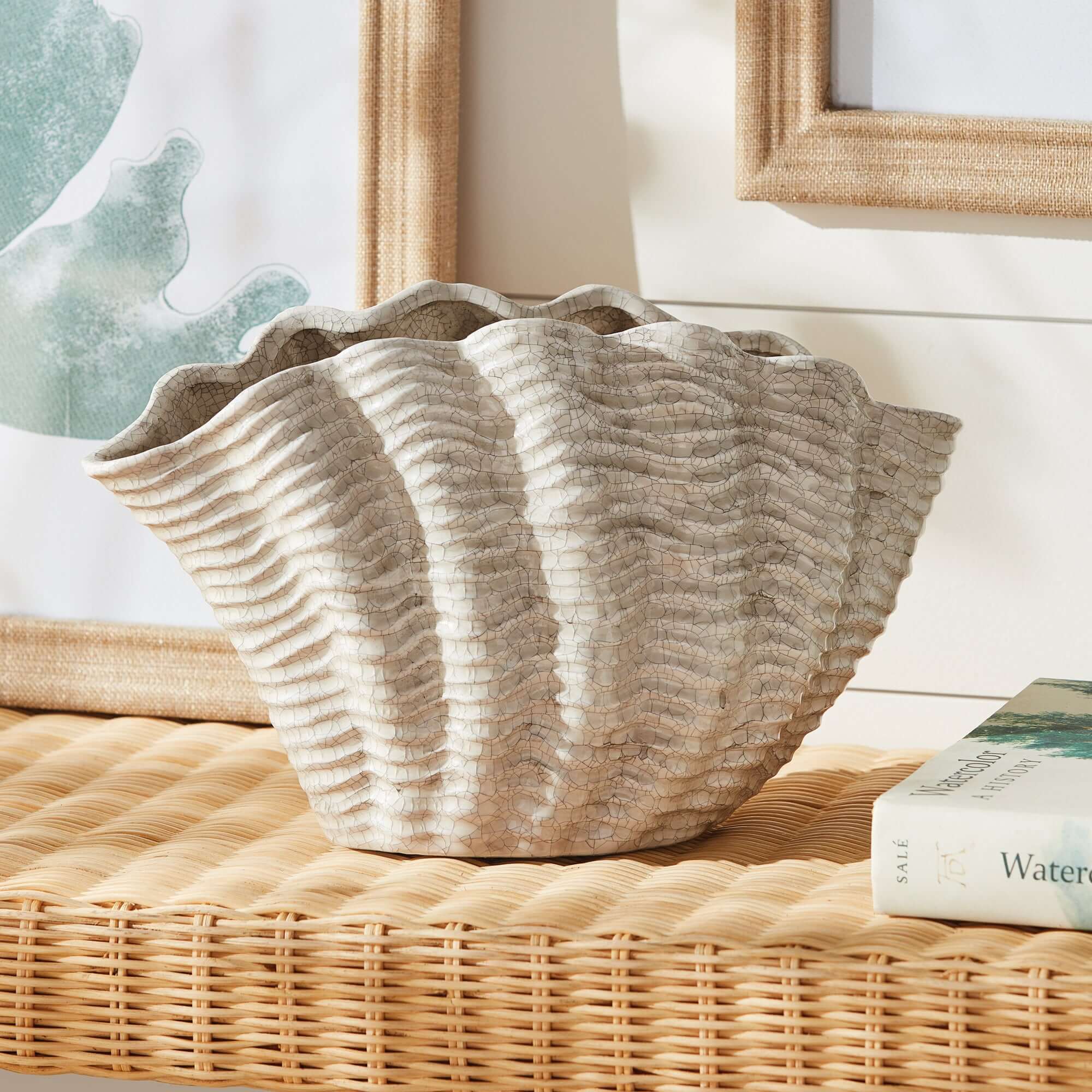 Textured ceramic shell shaped vase on a wicker surface with a blurred indoor setting
