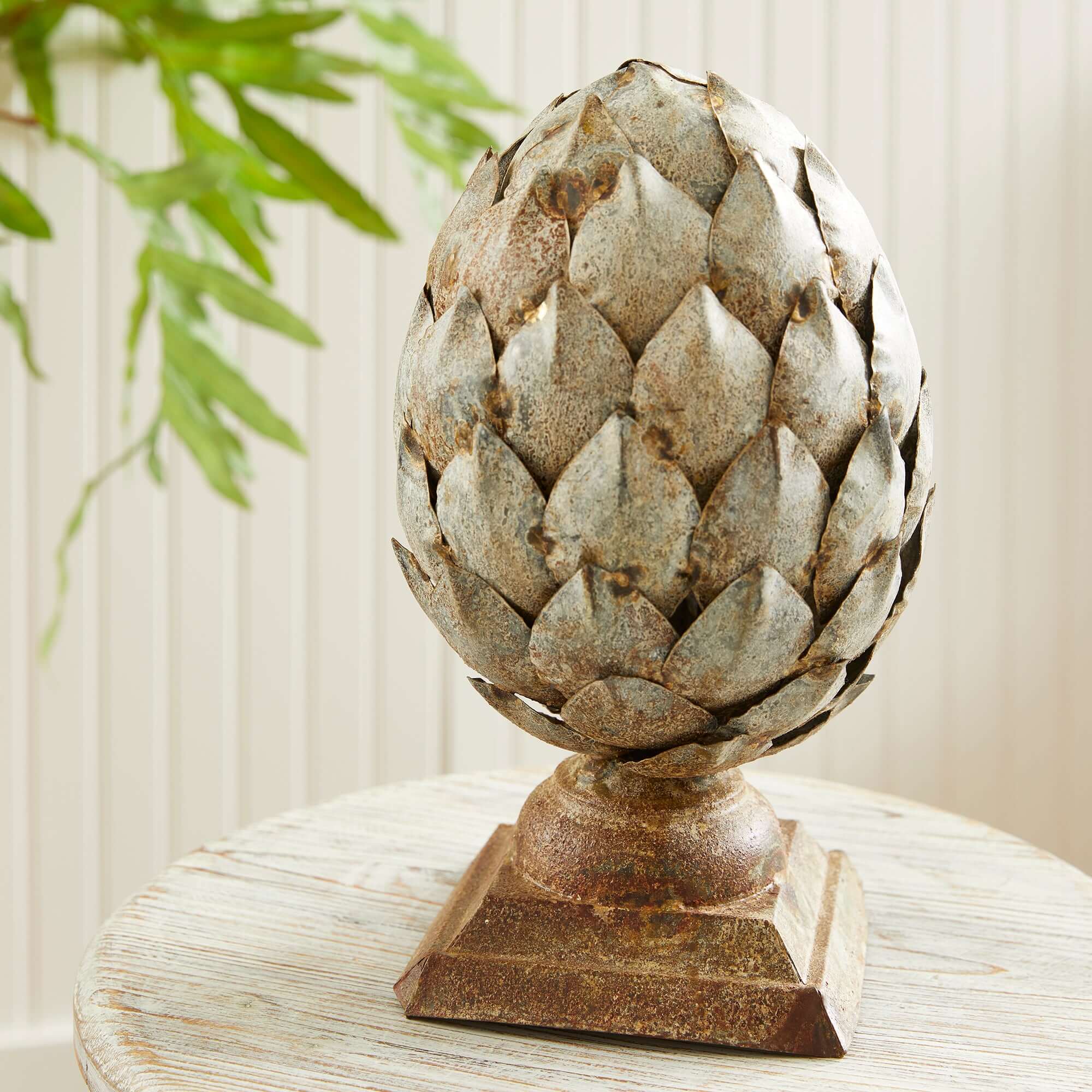 Decorative artichoke sculpture on a pedestal with a blurred plant in the background