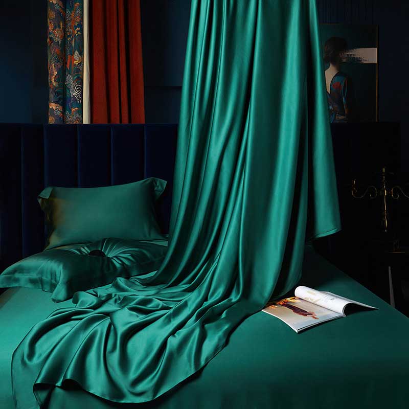 Teal satin sheet draped over a bed with a magazine on a dark background