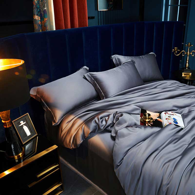 Gray bedding set on a bed with a dark blue headboard in a dimly lit room.