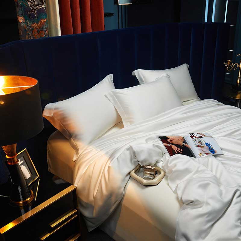 Neatly made bed with white pillows and duvet, nightstand with lamp and decor items.