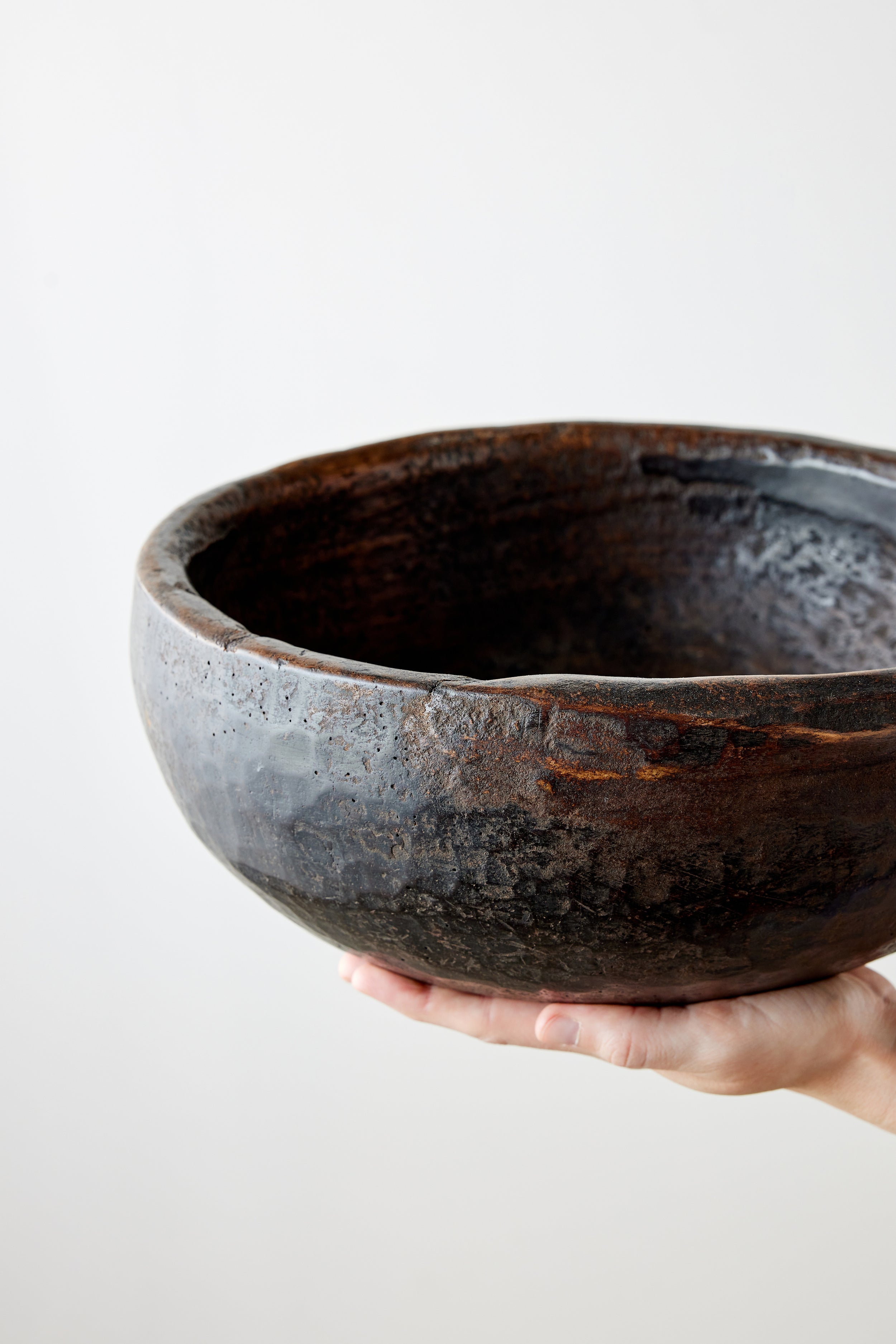 Hand holding a large, dark brown wooden bowl against a light background
