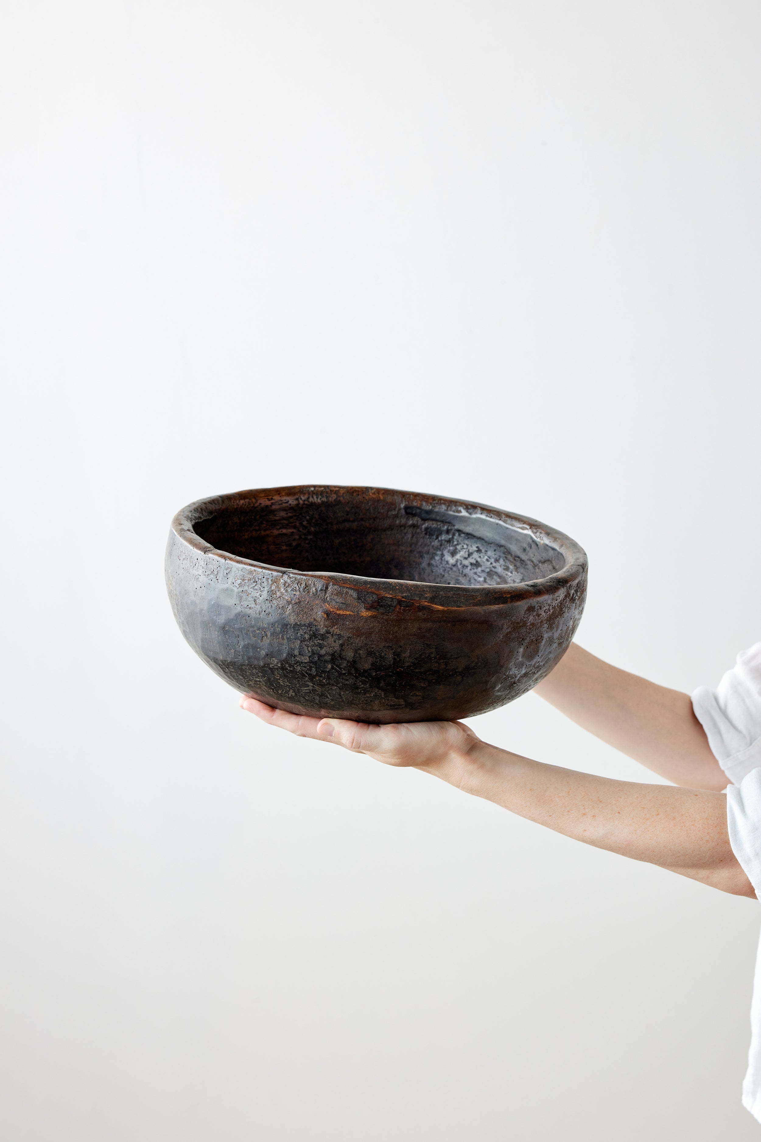 Person holding a large black wooden bowl against a white background