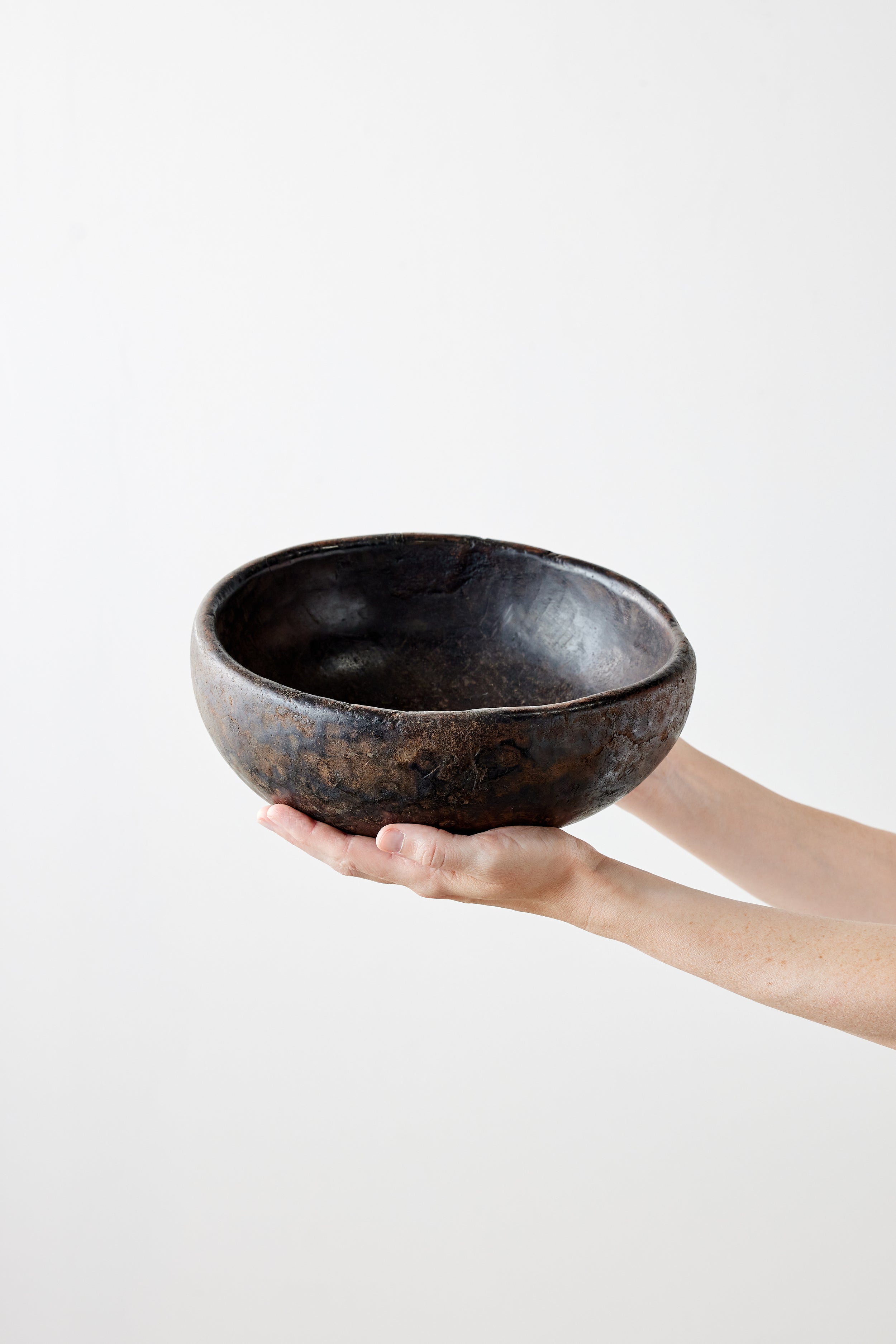 Person holding a black wooden bowl against a white background