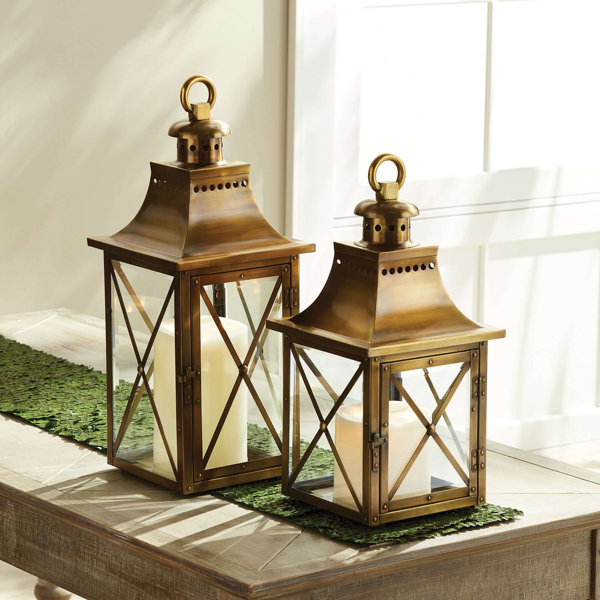 Two brass lanterns with candles inside on a table near a window.