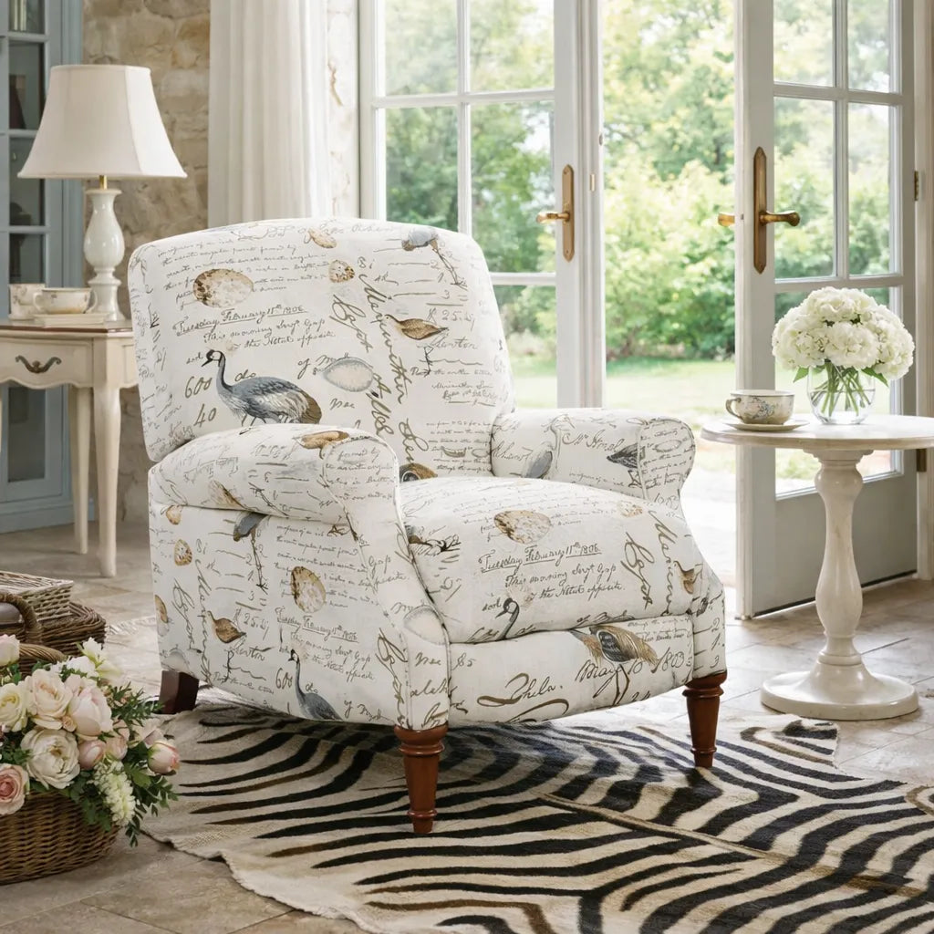 Patterned armchair in a room with large windows, flowers, and a lamp.
