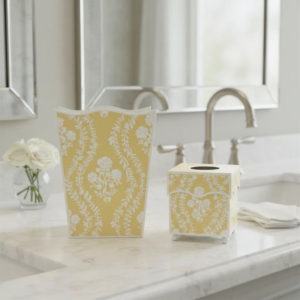 Butter yellow wastepaper basket and tissue box cover with white floral pattern on a marble bathroom countertop