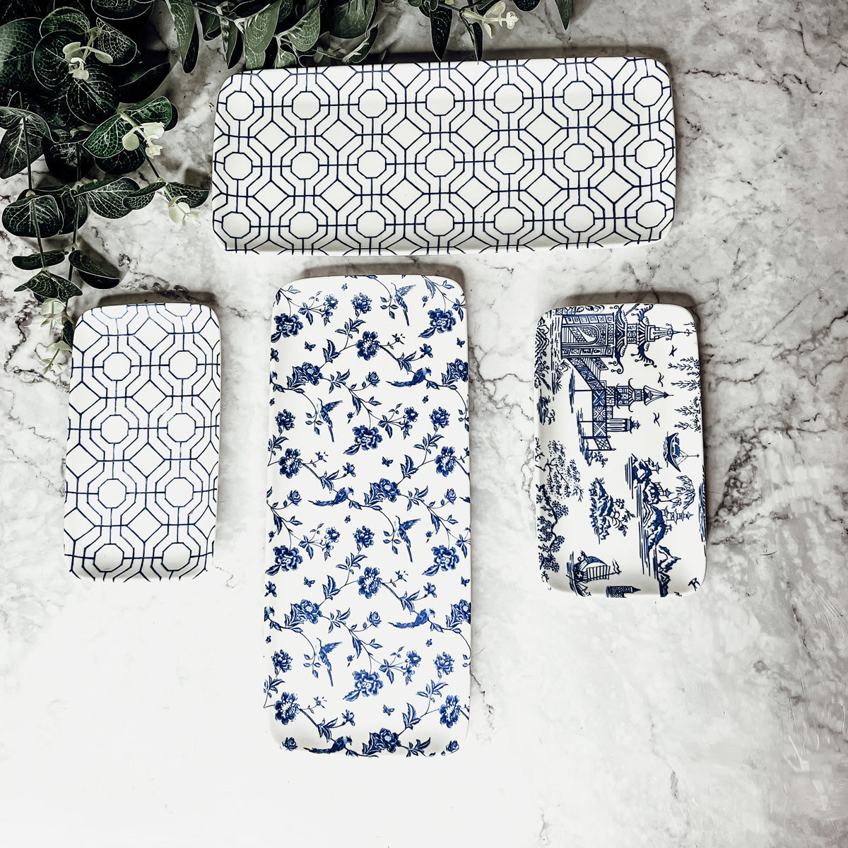 Set of four decorative serving trays with geometric, floral, and architectural toile patterns on a marble surface.