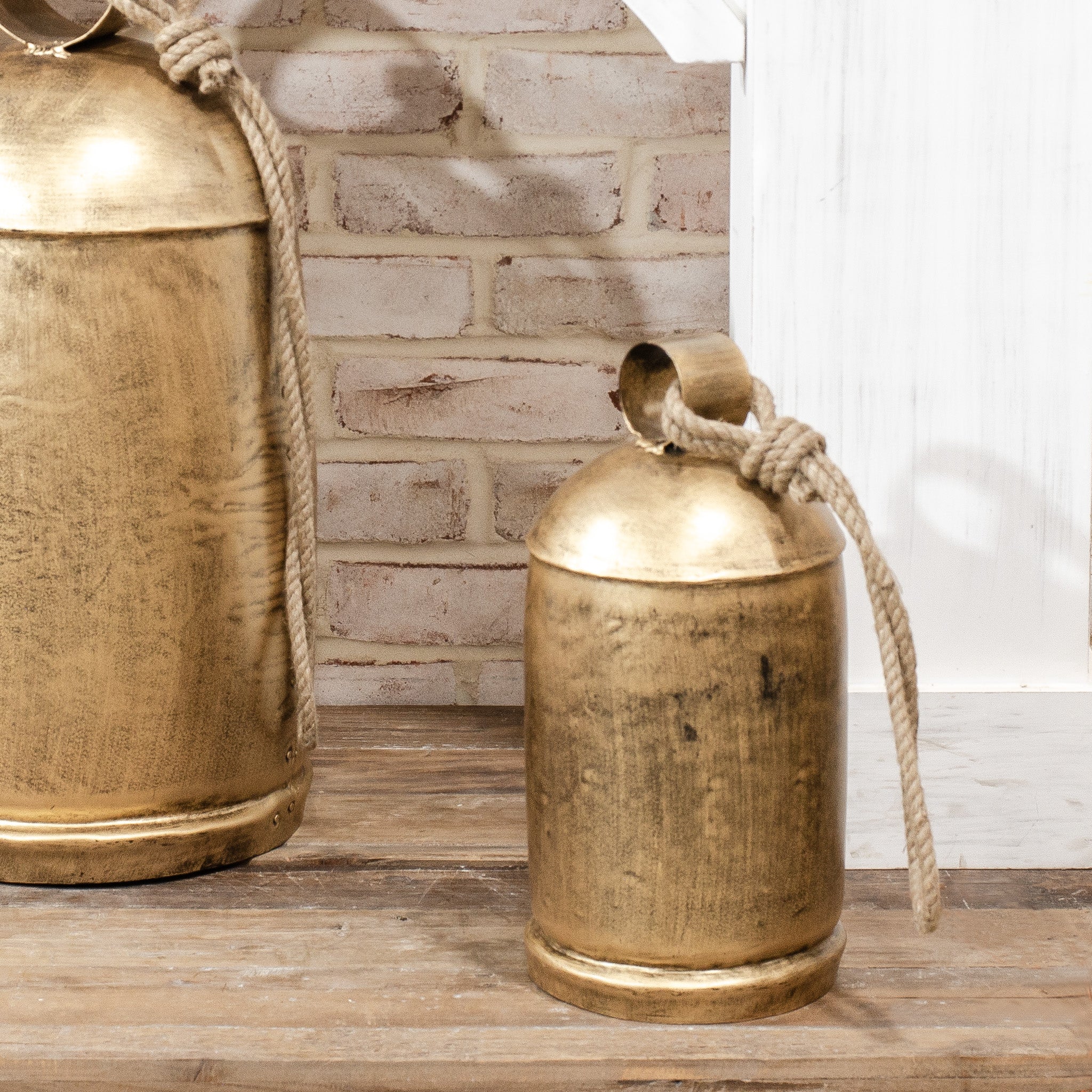 Two brass bells with ropes on a wooden surface against a brick wall.