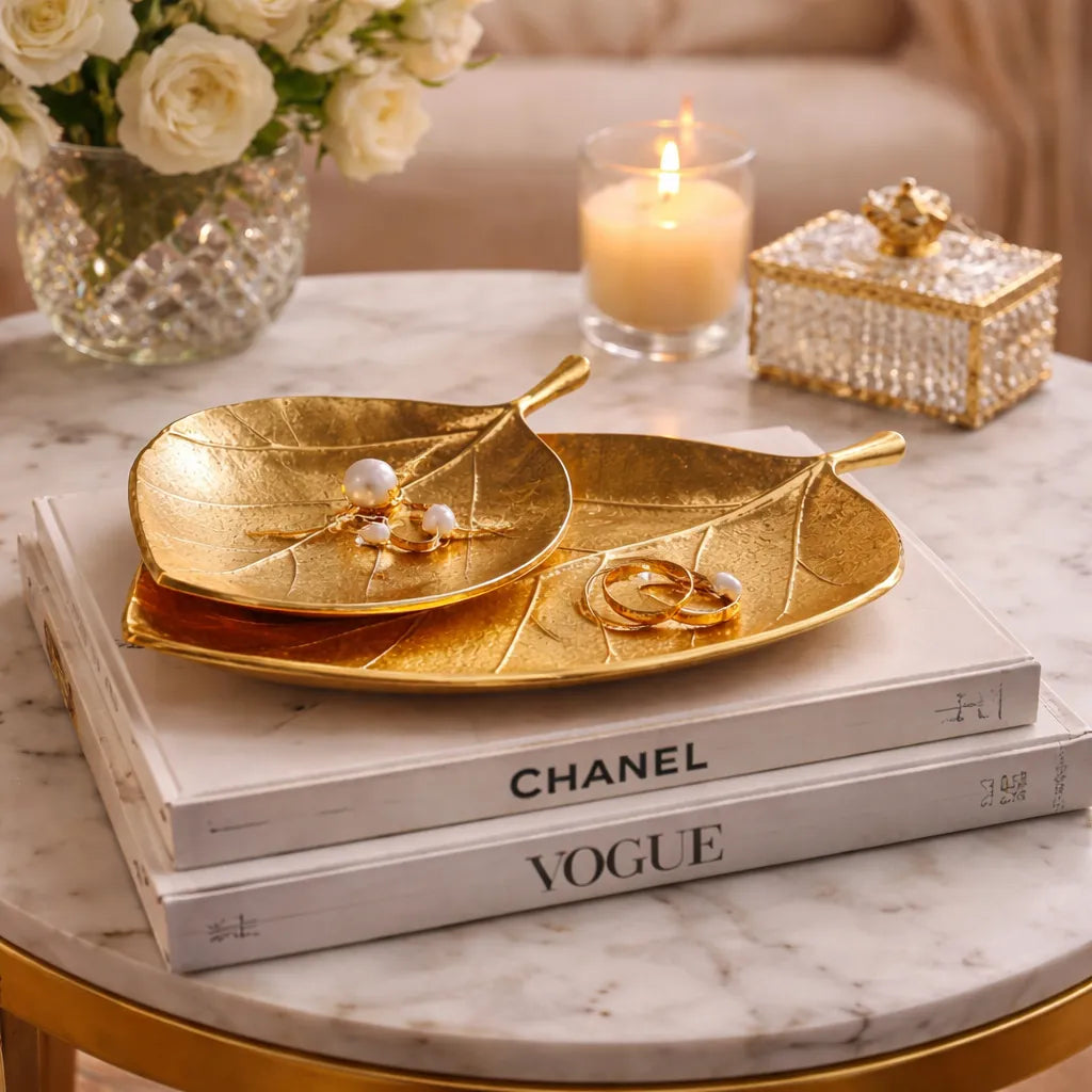 decorative gold leaf shaped trays on top of books with a candle and flowers in the background