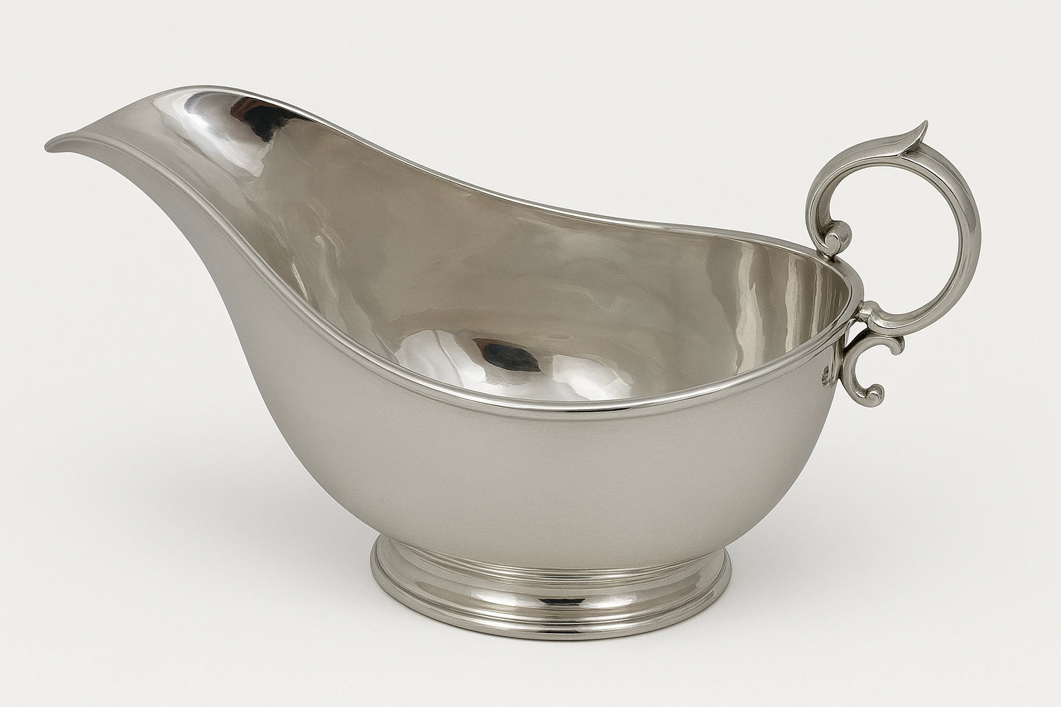 English silver plate sauceboat with engraved crest motif, shown in full side profile with curved spout and scroll handle