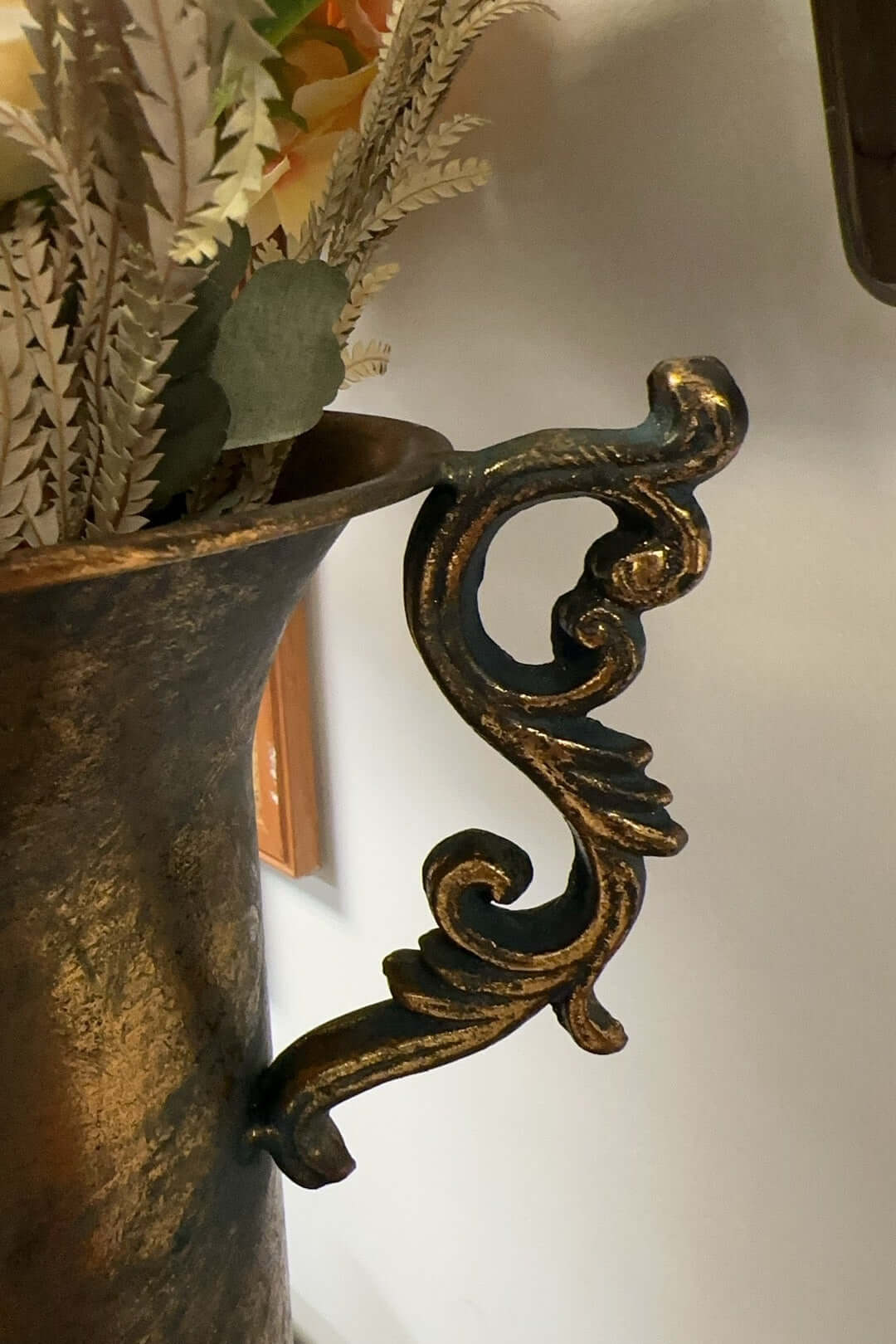 Decorative metal handle on a vase with a blurred floral background