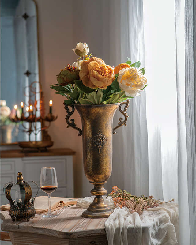Decorative metal french country vase with flowers on a table in a softly lit room.