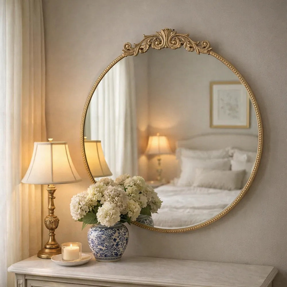 Decorative round mirror with gold frame on a wall above a table with a lamp and floral arrangement.