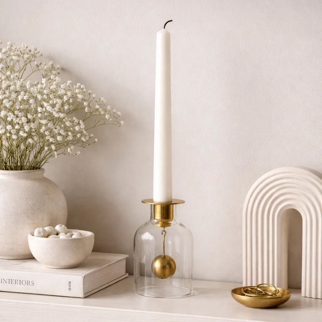 Klong Bell candlestick with mouth-blown clear glass base and matte brass bell styled on a minimalist Scandinavian shelf with neutral ceramics, brass accents, and soft white florals.
