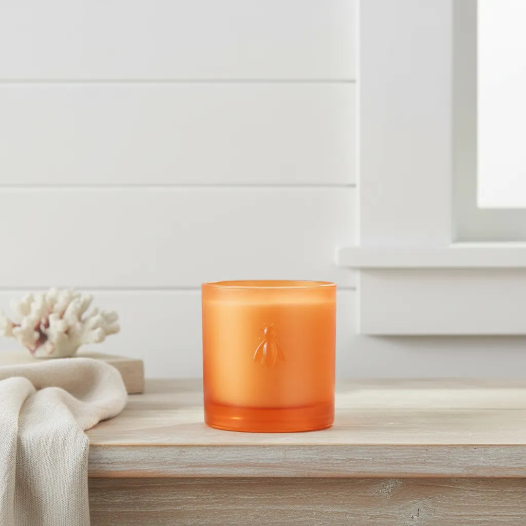 La Rochere Orange candle in a glass holder on a wooden surface with a white background