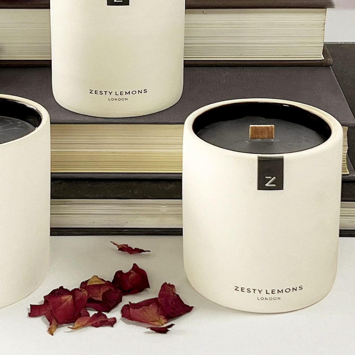 Candle with 'Zesty Lemons London' branding on a surface with books and dried flowers.