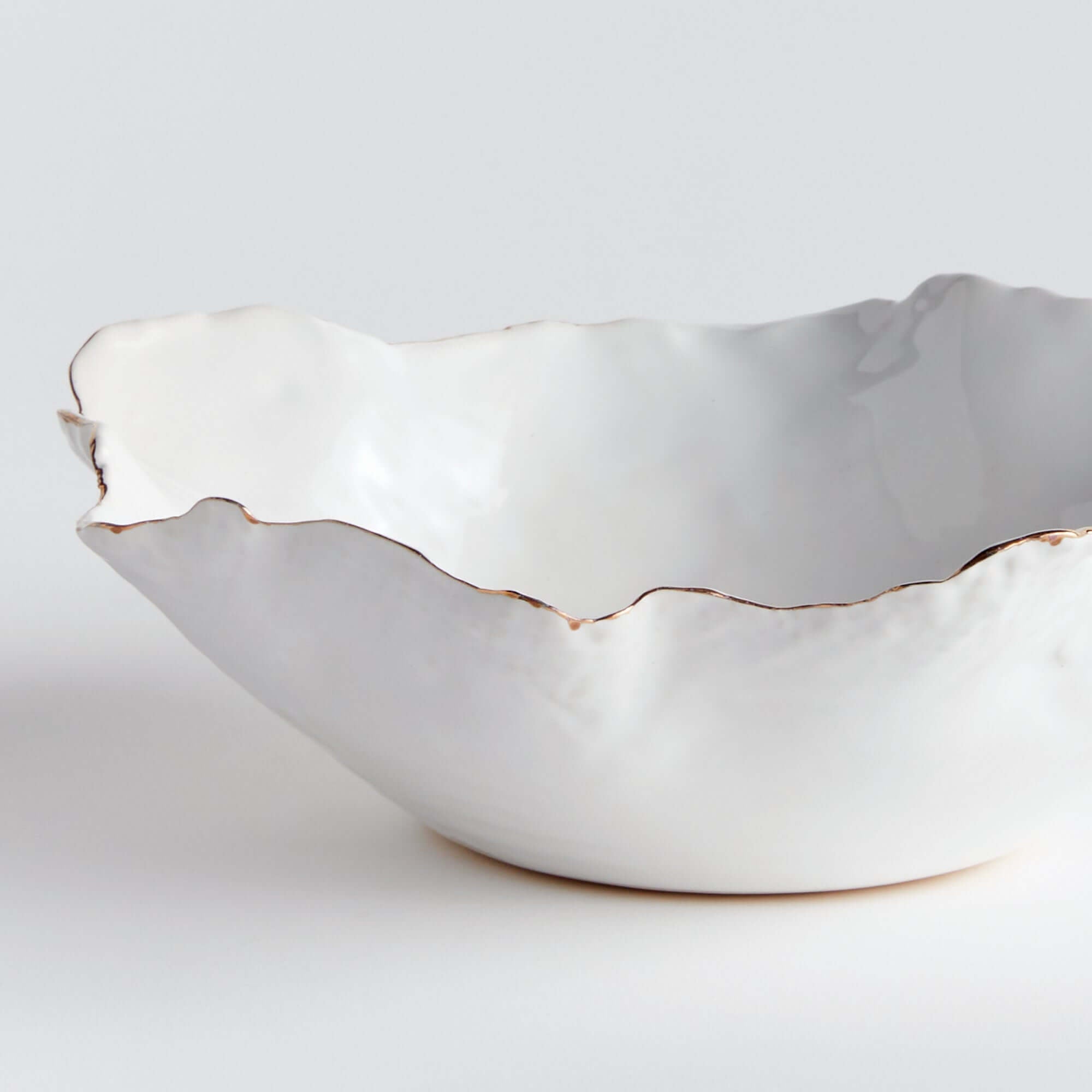 White ceramic bowl with scalloped gold edge on a light gray background