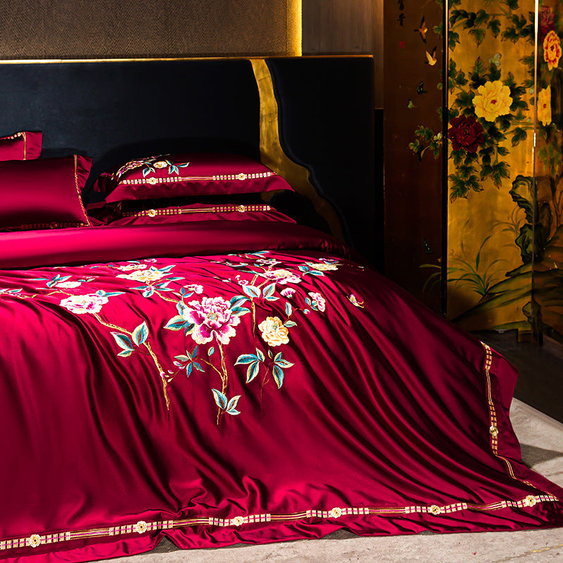Red embroidered bedding set on a bed with floral patterns in a decorated room.