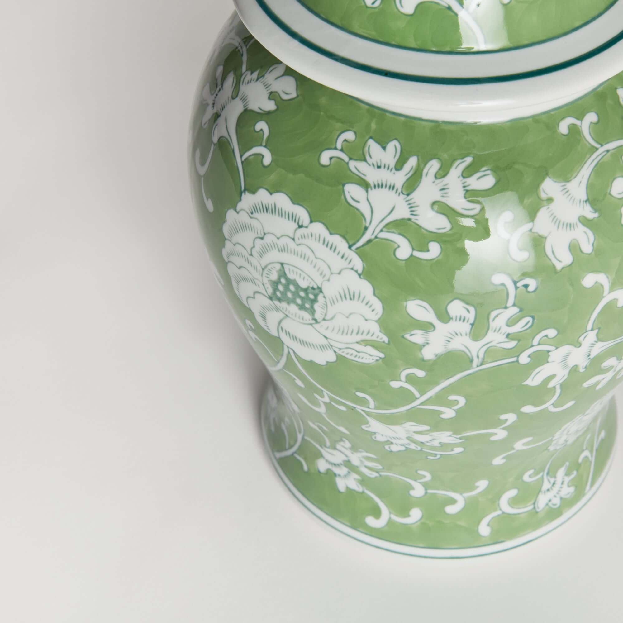 Green ceramic jar with white floral patterns on a light gray background