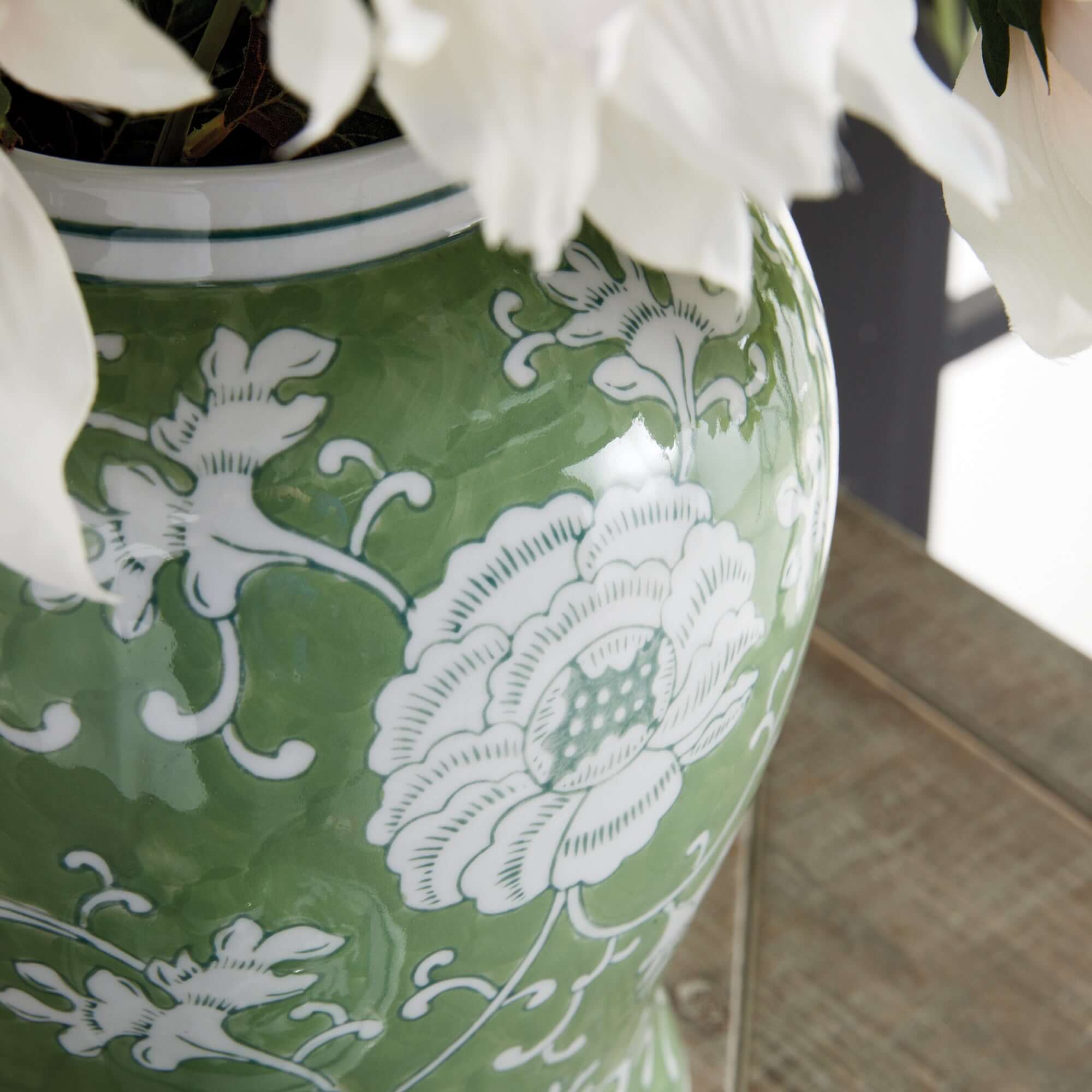 Close up of a green and white chinoiserie ceramic vase with white floral patterns and white flowers on top