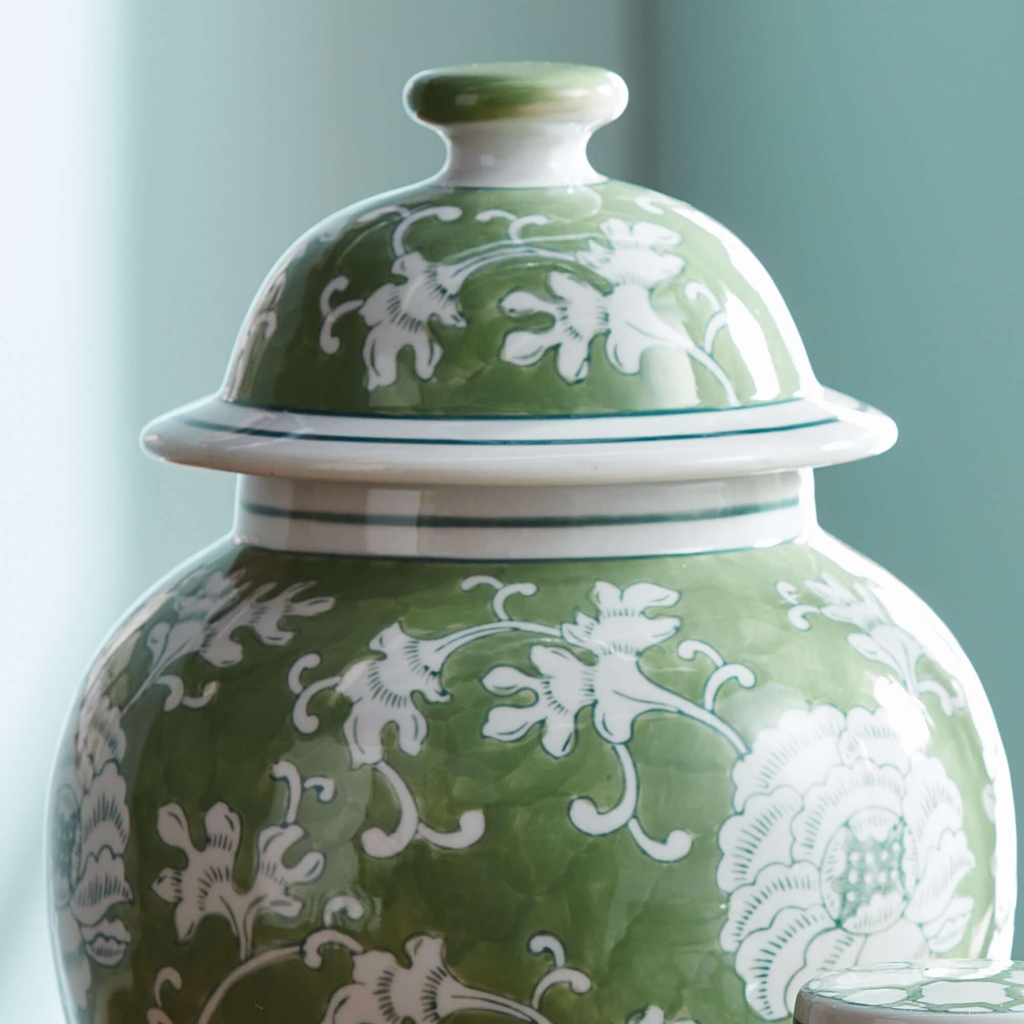 Green ceramic jar with white floral patterns on a light blue background